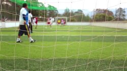 Goalkeeper watches players scramble for soccer ball in local football match (Net POV) Stock Footage