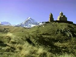 WS PAN Shot of symbol of church gergeti trinity church (tsminda sameba) with mount kazbegi and snowy peak, Georgia / Stepantsminda, Kazbegi, Georgia  Stock Footage