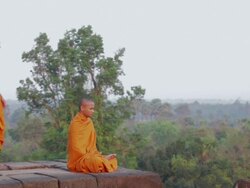 WS A Buddhist monk meditates and is joined by another who stands looking out at the sun rising above the jungle on an ancient temple in Angkor Wat / Siem Reap, Cambodia Stock Footage