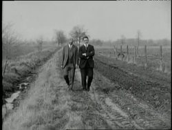 Henry Ford and Charles Sorensen walk together on a dirt track. News Clip