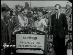 1946: AMERICAN ZONE, GERMANY: EXPORT SHOW: Export Show banner. People walking around outside exhibits. Boy driving small diesel open locomotive on track. Large crowd outside. People walking by Bavarian beer sign. People looking at dry goods, cloth. Instructional Video