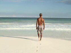 Man walking on sandy beach into the sea Stock Footage