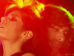 Handheld medium shot zoom young woman sings into microphone and dances as young man plays guitar behind her Stock Footage