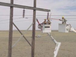 WS AERIAL Energy workers adjusting copper coil connected to powerline from safety of two cherry pickers / Hooker, OK, USA Stock Footage