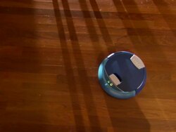 High Angle static - A small robotic vacuum cleaner sweeps a hardwood floor.   Stock Footage