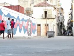 WS LA View of building and vehicle passing on steet with people and mural painting of amor cuerdoon wall / Havana, Cuba Stock Footage