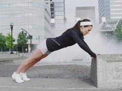 MS SLO MO Shot of young female jogger exercises by doing pushups on step at city fountain / Portland, Oregon, United States  Stock Footage