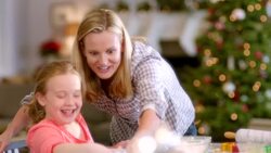 Mother helps happy young girl place Christmas tree-shaped cookie dough on baking sheet, hugs her proudly Stock Footage