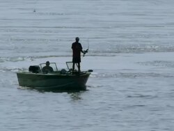 Man in boat on lake bow-fishing draws bow and fires arrow Stock Footage