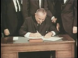 Dignitaries surround President Lyndon B. Johnson as he signs a bill. News Clip
