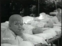 1935: MOSCOW, USSR, SOVIET UNION: State Day Nursery, baby having mouth checked. Nurse attending to baby at end of row of babies on cots. Baby w/ hand on chin. VS Toddlers learning rhythm exercises from nurse, 'dancing', walking up stairs, sliding. Instructional Video