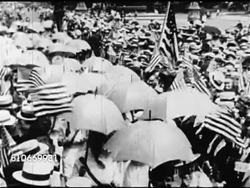 1920: WOMEN'S SUFFRAGE: HA WS Women w/ shade umbrellas walking through crowd waving US flags. VS Suffragettes on sidewalk selling newspapers, one w/ chest banner 'Vote wo' Women's Rights, vote. Instructional Video
