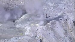 Smoke billows from a volcano where a volcanologist prepares testing equipment . Stock Footage