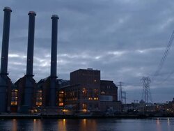 Electrical power plant with three smokestacks alongside river at dusk - framed to include high tension power lines Stock Footage