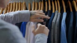 Young man flips through Sale rack and picks out t-shirt in clothing store Stock Footage