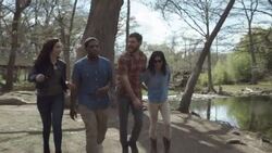 Group of friends walk through public park talking and laughing by riverside Stock Footage