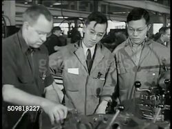1944: JONES & LAMSON MACHINE CO.: ASIAN ENGINEER: INT MS Middle aged white man showing machine to two young Asian engineers. CU Lathe machine, liquid over spinning metal piece. MS Asian men talking. Factory workers, Springfield, Vermont Instructional Video
