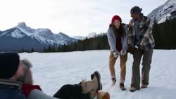 Young couples sledding in snowy field below mountains Stock Footage