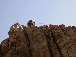 Tilt shot of a rock-climber beginning his descent from the top of a cliff. Stock Footage