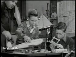 1946: FAMILY:  Father helping two sons assemble model airplane on table. Father explaining something to younger boy (no SOT). Mother making frosting w/ two daughters in kitchen, girls icing cake. Brunette girl w/ flour in bangs smiling. Iconic. Instructional Video