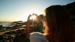 Caucasian female frames sunset on beach into heart shape Stock Footage