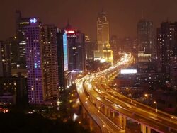 TL of highway with busy traffic between high rise buildings in Shanghai at night. Static shot. Stock Footage