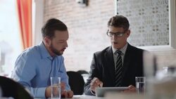 Business partners study graphs and figures on tablet computer and discuss paperwork Stock Footage