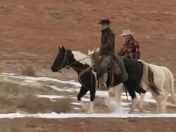 TS Three cowboys trotting on horses in front of red rock landscape kicking up snow as they go / Shell, Wyoming, United States Stock Footage