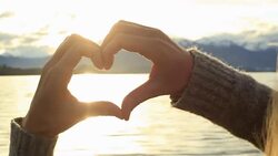 Female makes heart shape finger frame on lake mountain landscape Stock Footage