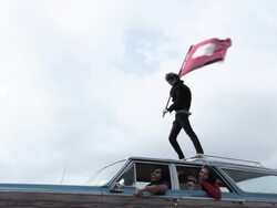 Teenage boy standing on car roof with friends inside car Stock Footage