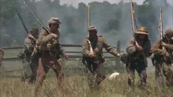 Confederate soldiers carry their rifles over a fence, then run across a battlefield. Stock Footage