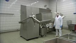 A technician works in a sausage making plant where a machine dumps ingredients into a vat. Stock Footage