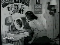 1945: TEENAGE GIRLS: DRAMATIZATION: Teenage girl sitting at vanity in bedroom, putting on lipstick, staring at movie star photographs (8x10s) on wall above vanity (MacMurray, Peck, Ladd, Sinatra) Instructional Video
