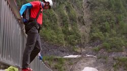BASE jumper descends from high concrete dam to valley below Stock Footage