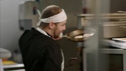 In restaurant kitchen, head chef chats with kitchen staff and places pan in oven Stock Footage
