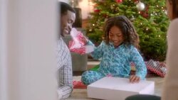 Smiling parents watch as girl unwraps Christmas present and admires new pink sweater (dolly-shot) Stock Footage