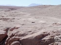 MS PAN Shot of deserted sandy landscape with water flowing through small canyon and primitive stone looking structure Stock Footage