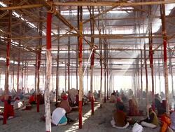 Suns rays slant through ricketty wooden scaffolding as devotees sit on ground below around fires, involved in religious ritual. Kumbh Mela, India Stock Footage