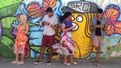 Brazilian friends lean against graffitied wall and text on smartphones Stock Footage
