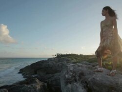 Young woman standing on rocks by the sea with breeze blowing her dress Stock Footage