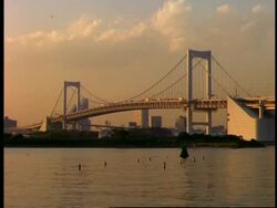 WA view across water to Rainbow suspension bridge, bathed in orange dusk light, Tokyo, Japan Stock Footage
