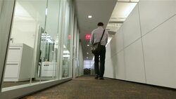 Fired employee walks despondently away down office hallway with box of belongings Stock Footage