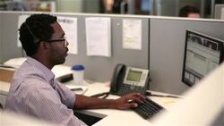 Multitasking office worker talks on headset, clicks through multiple computer windows (dolly shot) Stock Footage