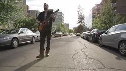 Cool young man playing guitar walking down urban street Stock Footage