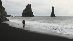 A man dodging waves on a black volcanic sand beach  near Vik on Iceland's south coast. Stock Footage