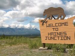 MS Shot of Wooden Welcome to Haines Junction roadside sign with wooden black bear and mountain range in back side on Haines Junction near Kluane National Park and Reserve / Haines Junction, Yukon, Canada Stock Footage