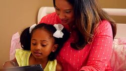 MS Smiling mother and daughter sitting on bed reading book together on digital tablet Stock Footage