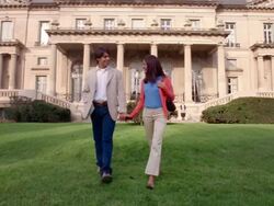 Wide shot young couple holding hands and walking on lawn in front of mansion / servants standing in background Stock Footage