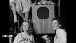 1950: LARGE CITY COMMUNITY COURT: NIGHT: Teenagers slow dancing together inside fenced basketball court, female teens standing by portable speaker, young teens sitting in bleachers. VS Dancers, clothing varies from rolled jeans to below the knee skirt Instructional Video