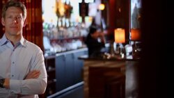 A bartender serves a drink to a patron as a restaurant owner stands nearby. Stock Footage